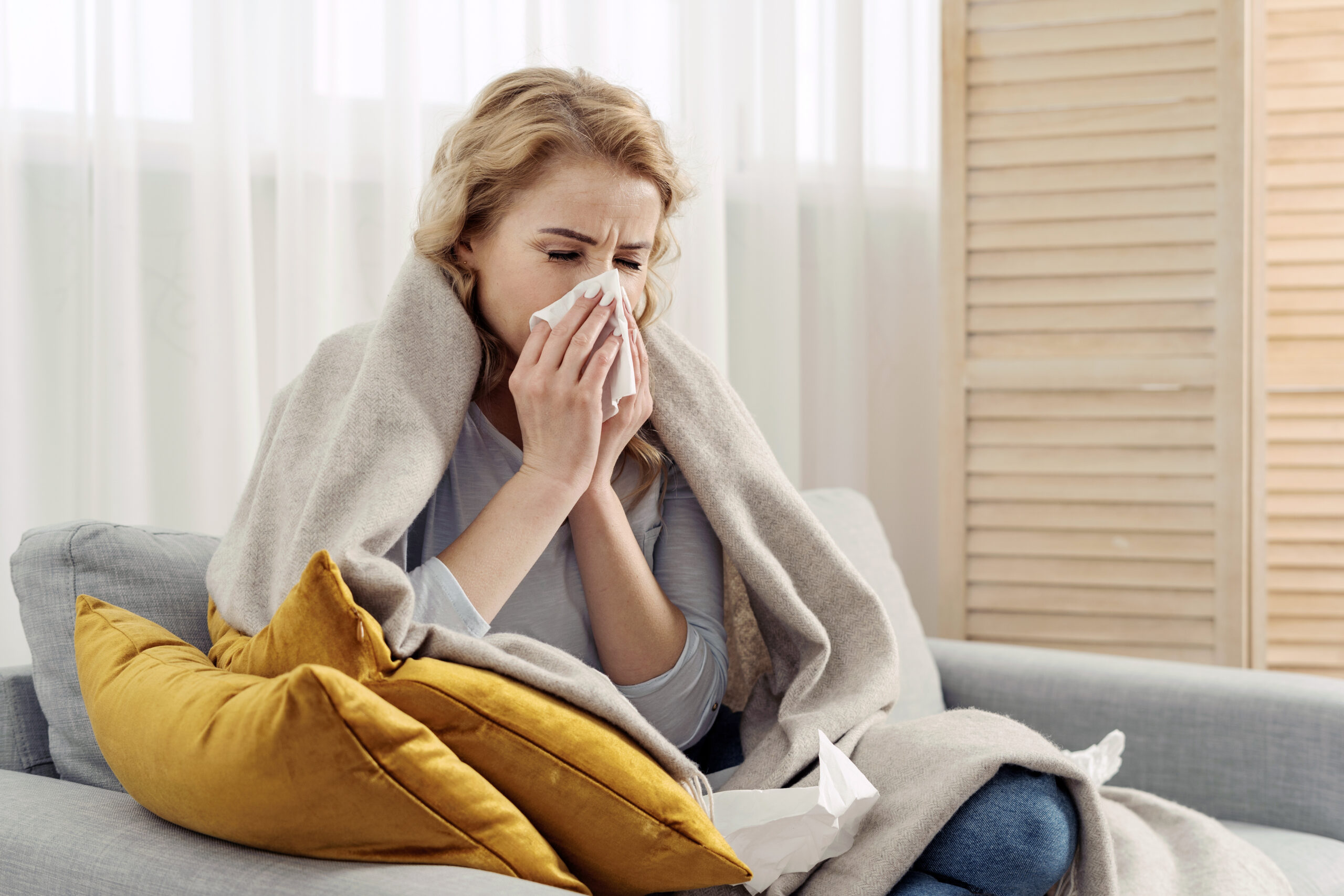 sick woman on the couch and blowing her nose